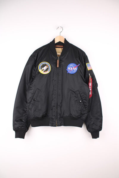 Black Alpha Industries NASA bomber jacket with zip-through fastening, two side pockets and one arm pocket, ribbed cuffs and hem, NASA/USA themed patches on the chest and sleeves, leather zip-pulls and a 'remove before flight' tag.